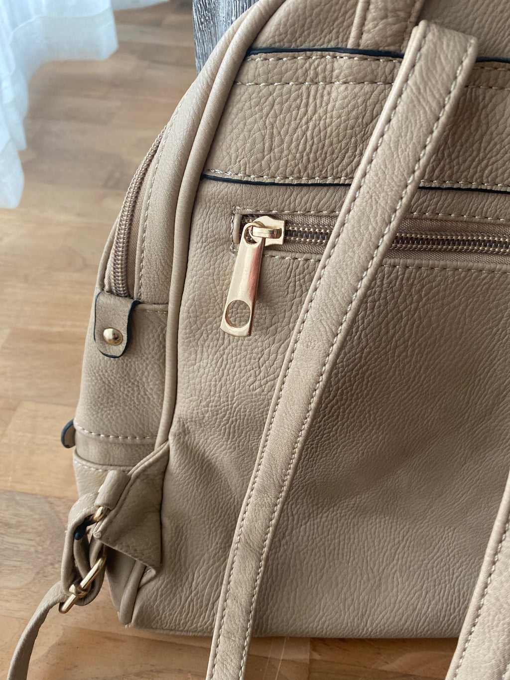 Beiger Damenrucksack in Lederoptik mit goldfarbenen Reißverschlüssen und Fronttasche auf weißem Hintergrund. Detailansicht