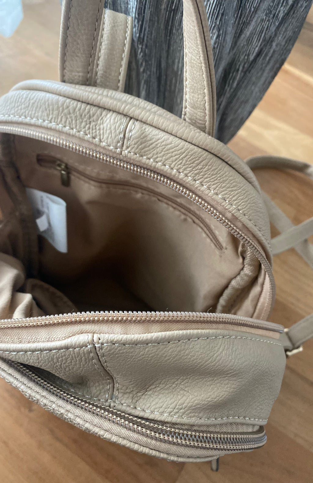 Beiger Damenrucksack in Lederoptik mit goldfarbenen Reißverschlüssen und Fronttasche auf weißem Hintergrund. Innenseite