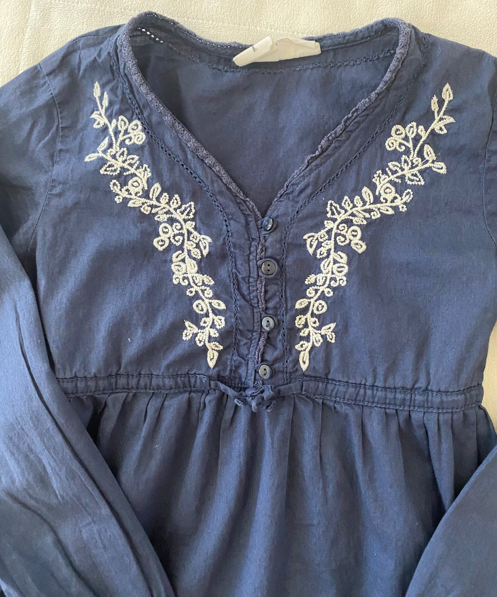 Detailaufnahme der weißen Stickerei und Knopfleiste eines blauen H&M Mädchen Kleids Größe 134