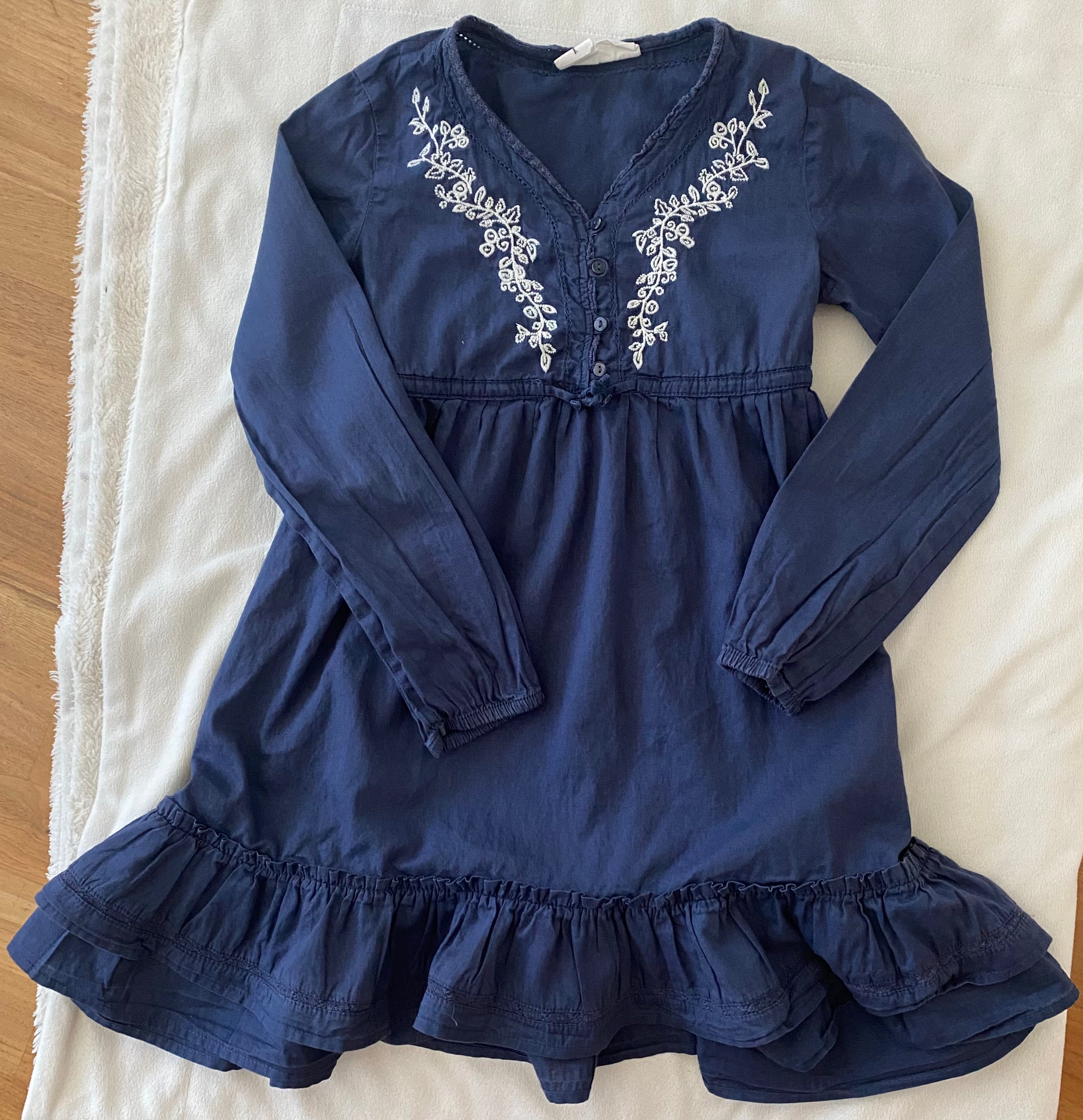 Blaues H&M Mädchen Kleid Größe 134 mit weißer Stickerei, langen Ärmeln und Volantsaum flach liegend