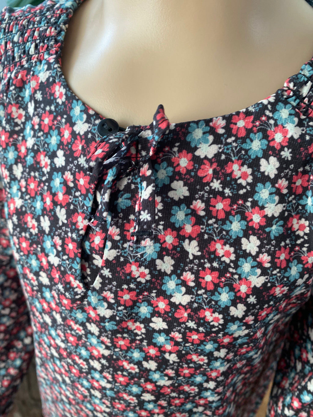 Heidi Detailaufnahme eines Mädchenkleids mit floralem Muster, Schleife und Knopfleiste im Brustbereich