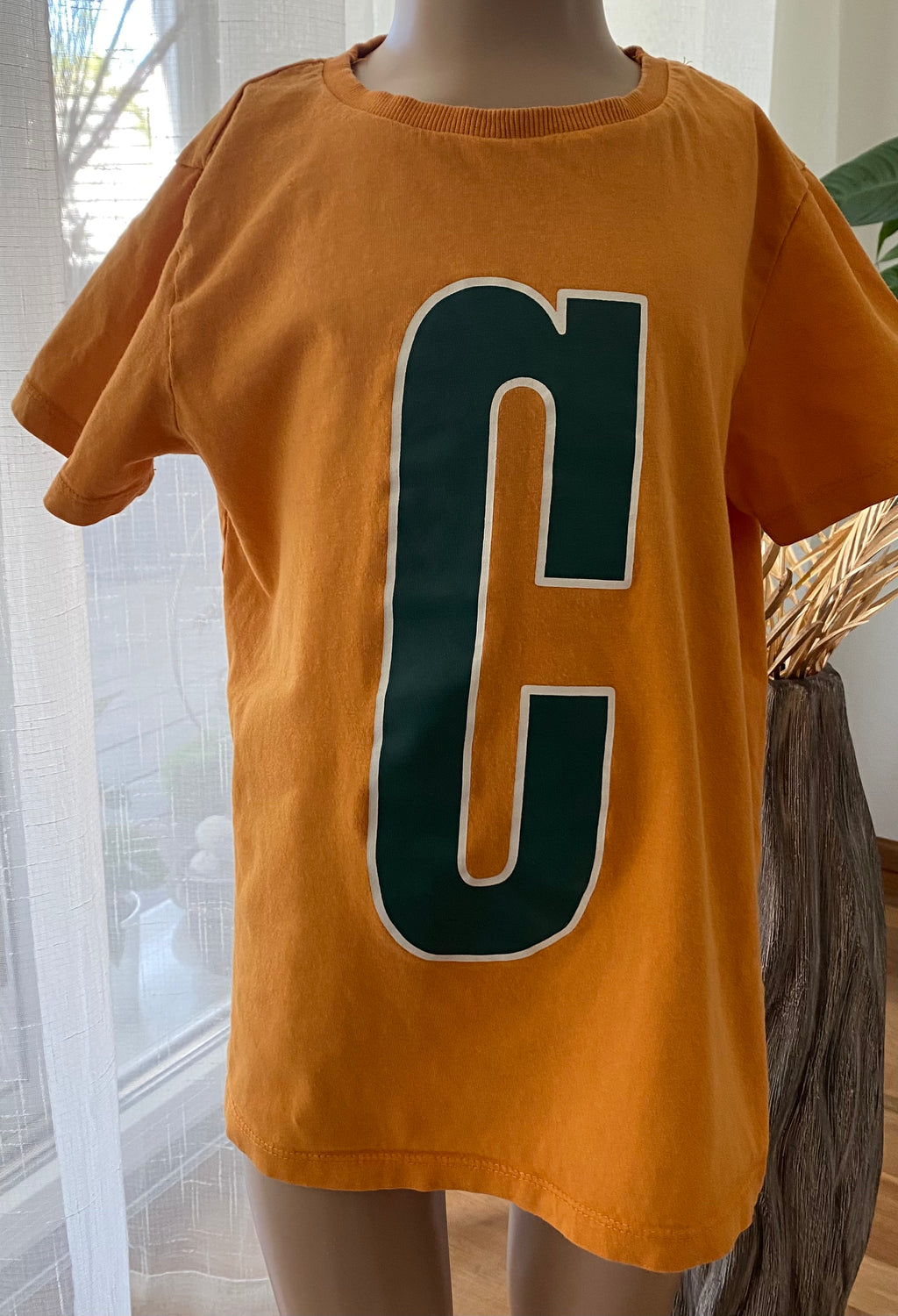 Jungen T-Shirt von NAME IT in Orange Größe 134–140 mit großem grünem Buchstaben C auf der Vorderseite, präsentiert auf einer Schaufensterpuppe