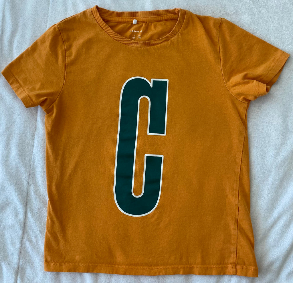 Orangefarbenes Jungen T-Shirt von NAME IT Größe 134–140 mit großem grünem Buchstaben C auf der Vorderseite, flach liegend fotografiert