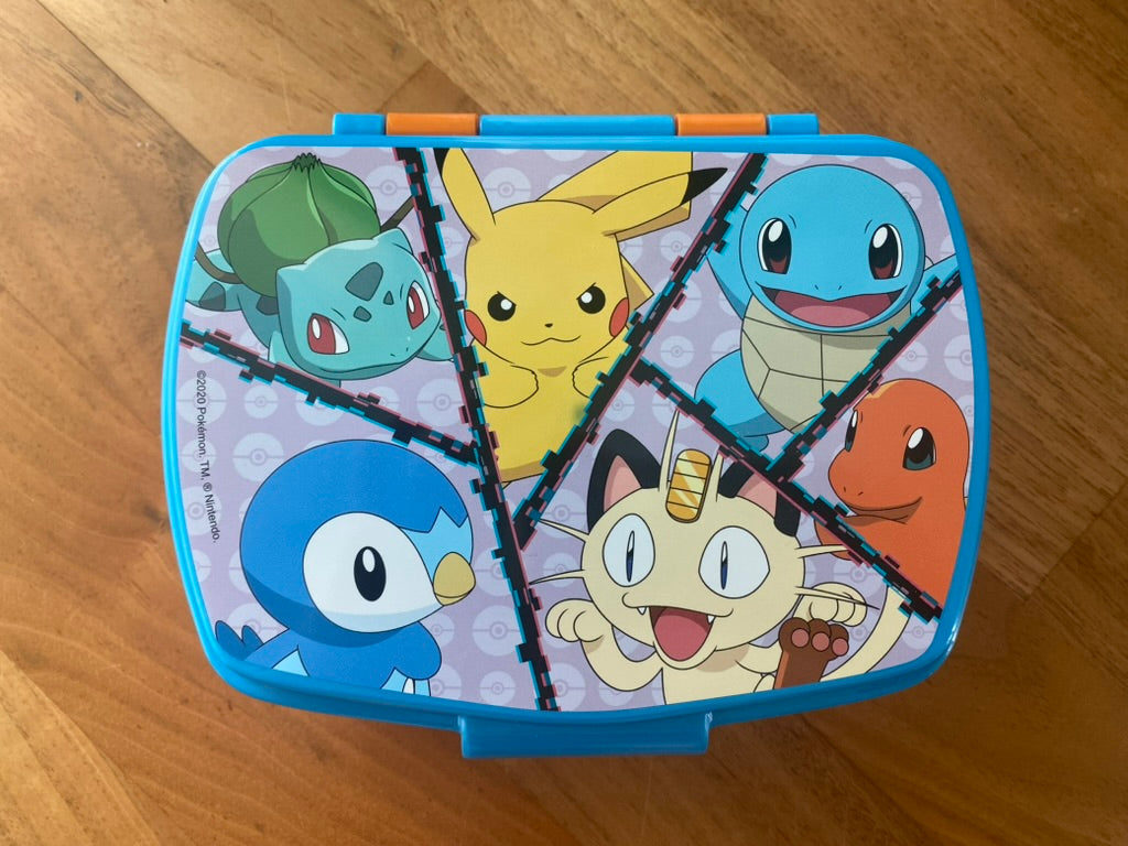 Pokémon Snackbox mit Pikachu, Schiggy, Glumanda, Bisasam, Mauzi und Plinfa auf Holztisch fotografiert Vorderseite