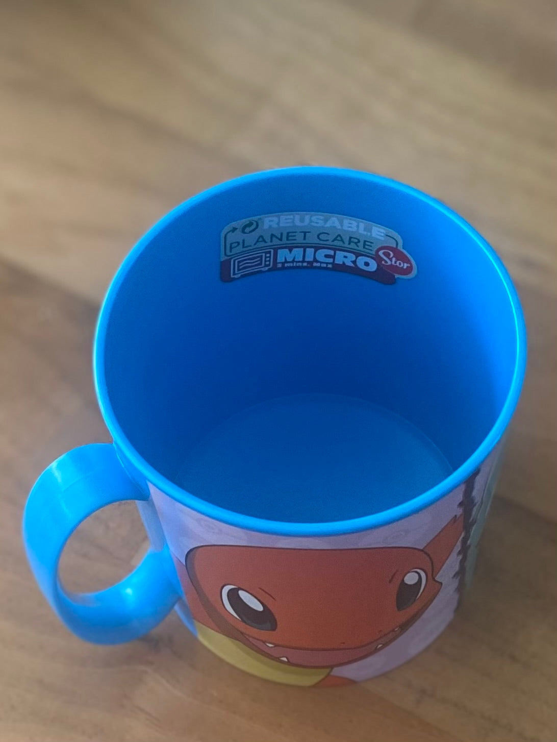 Blauer Pokémon Kinderbecher mit Schiggy Motiv und Henkel auf Holzuntergrund. Innenansicht