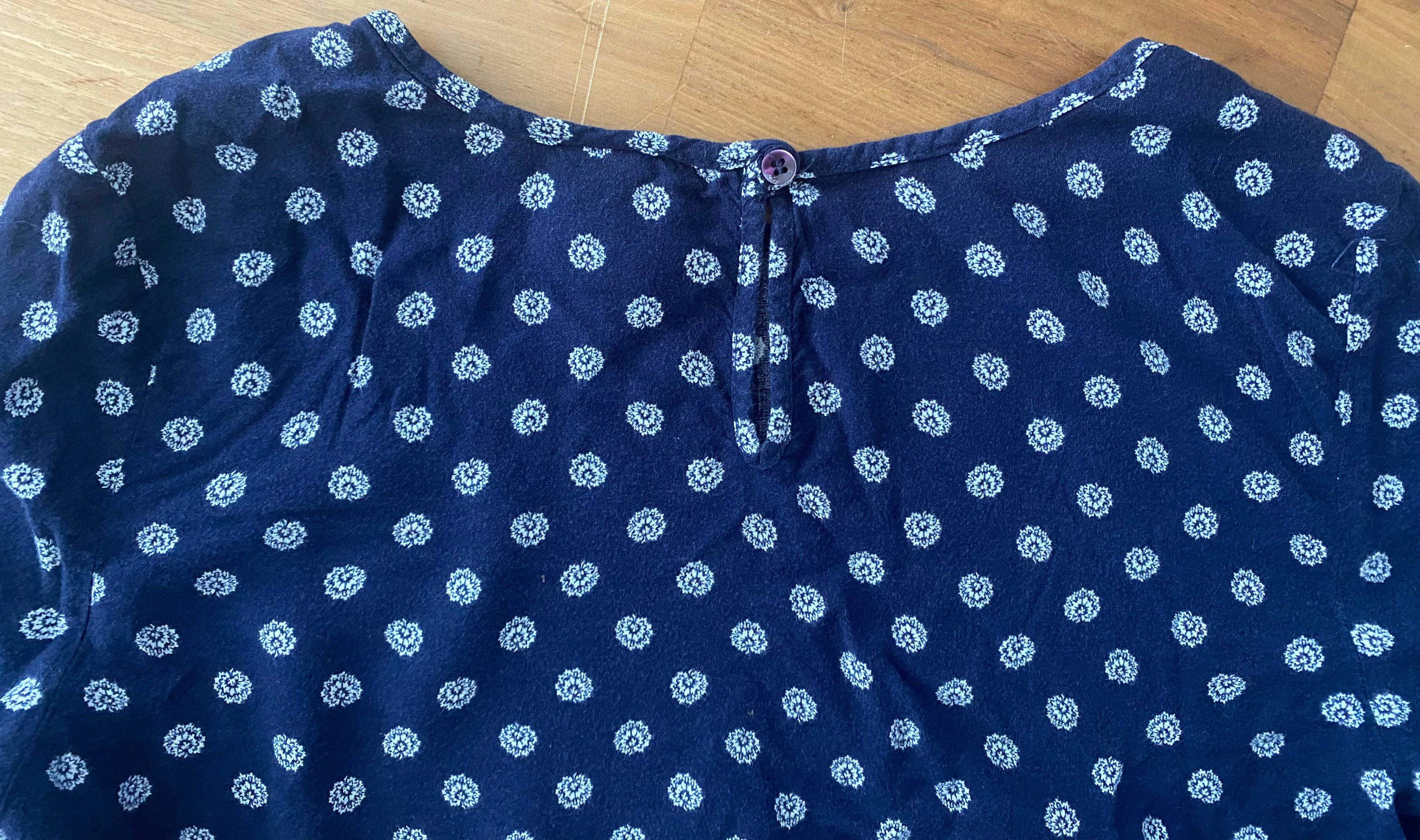 Detailfoto des rückseitigen Knopfverschlusses am dunkelblauen gemusterten Blusenshirt.