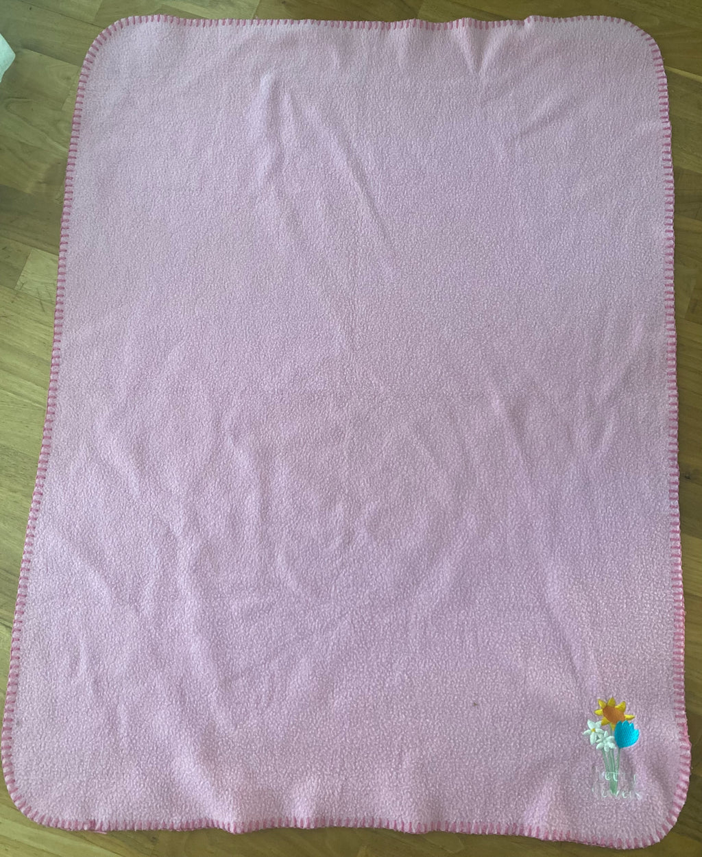Rosa Babydecke aus weichem Fleece mit dekorativer Blumenstickerei in der Ecke. Kuschelige Kinderdecke mit eingefasstem Rand, ideal für Kinderwagen, Bettchen oder gemütliche Kuschelstunden. Vorderseite