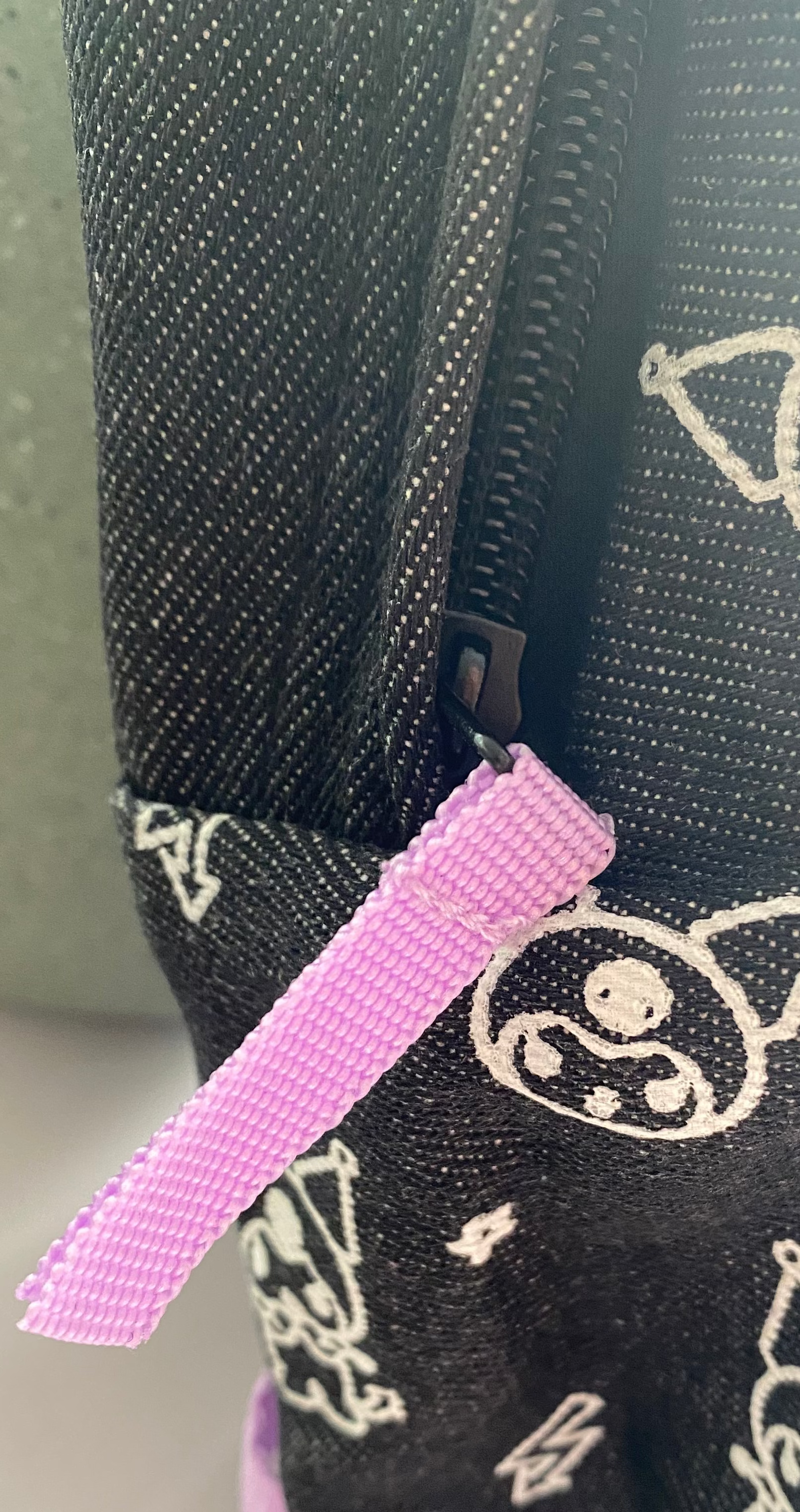 Schwarze Fronttasche des Kuromi Rucksacks mit lilafarbener Zipper-Schlaufe und KUROMI Label