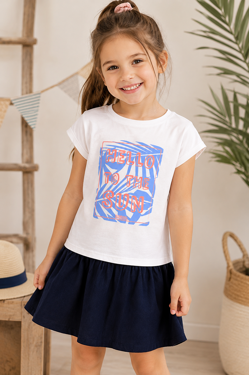Fröhliches Mädchen trägt ein weiß-blaues Sommerkleid mit „Hello to the Sun“-Print in einem hellen, sommerlichen Ambiente.