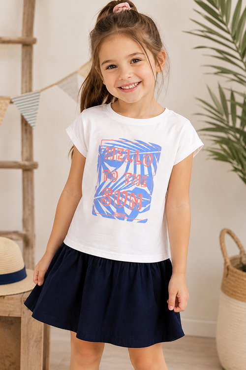 Fröhliches Mädchen trägt ein weiß-blaues Sommerkleid mit „Hello to the Sun“-Print in einem hellen, sommerlichen Ambiente.